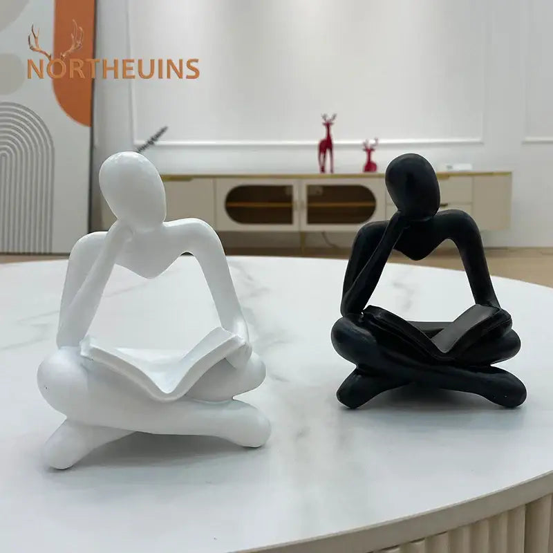 White and black abstract resin book figurines depicting seated human figures in meditative pose for office decorbites decor