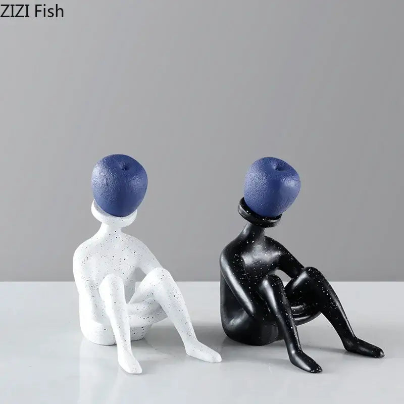 Two minimalist abstract thinker resin figurines with speckled black and white bodies and blue apple heads for decorbites decor