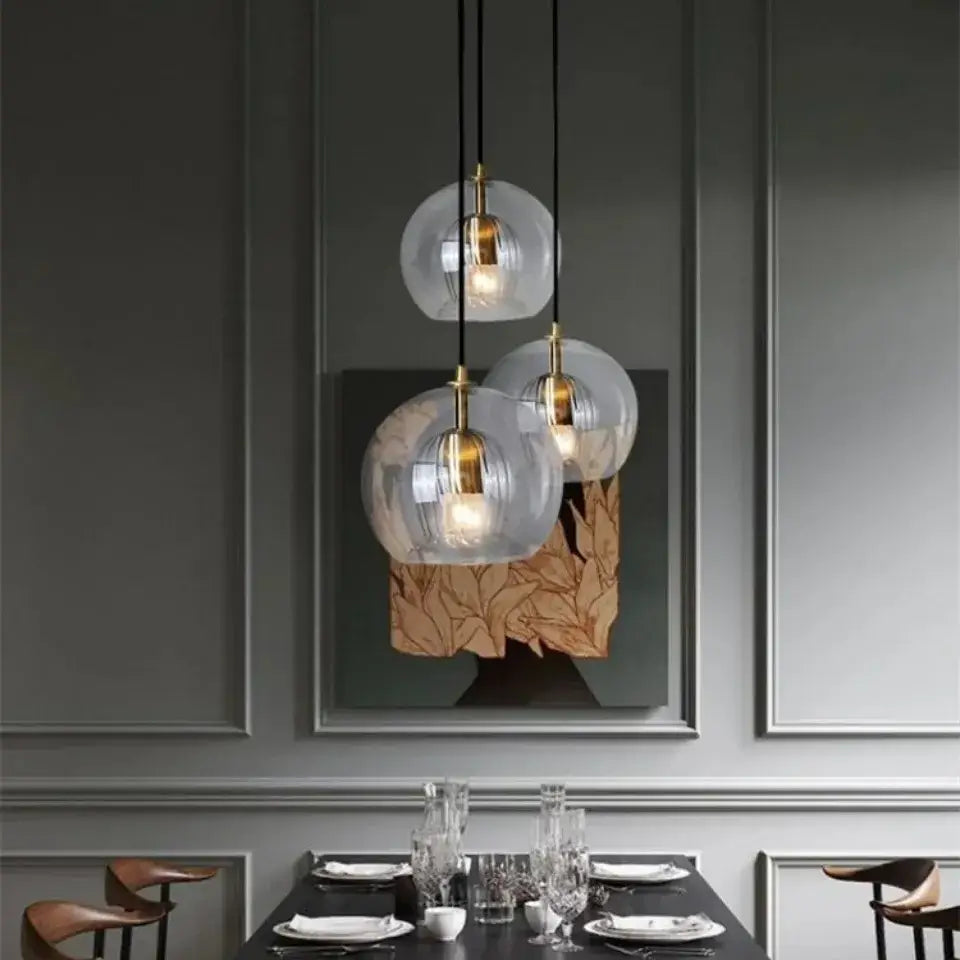Modern amber and clear glass pendant light with brass accents hangs above a dining table as a kitchen gold globe pendant light
