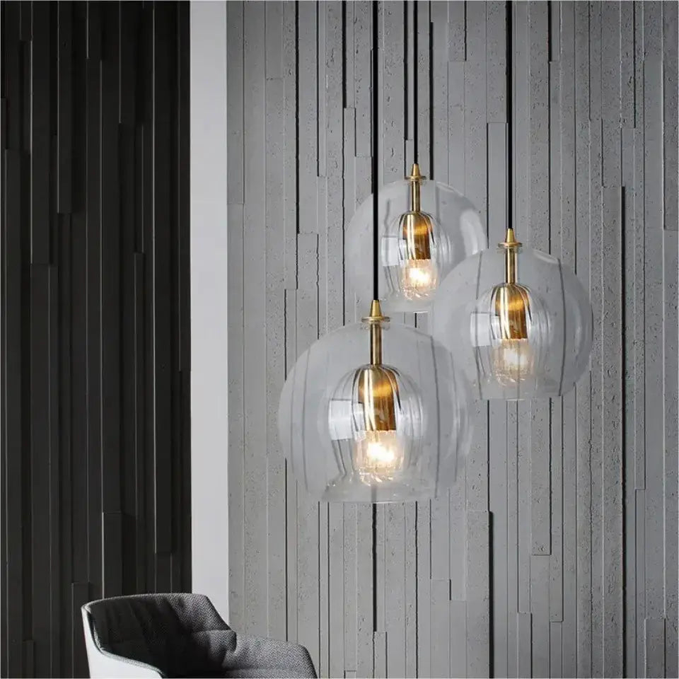Three modern amber and clear glass pendant lights with brass accents hang as kitchen gold cord pendant lights