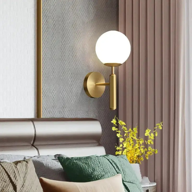 Gold-toned spherical wall sconce with frosted glass globe complements amber and cream glass pendant light for dining room