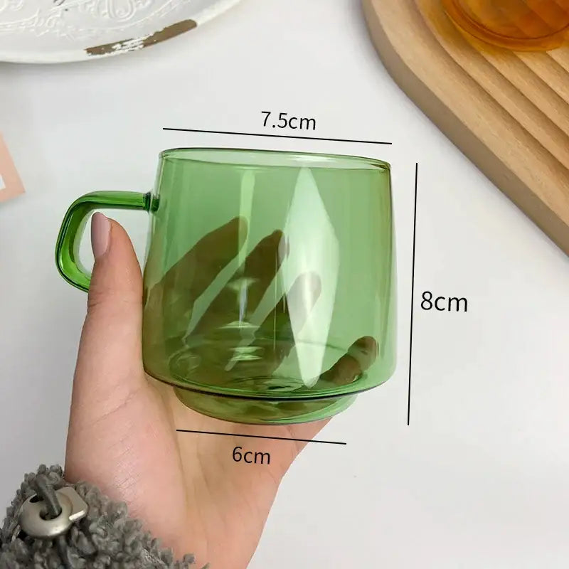 A translucent green decorbites glass coffee mug with matching handle held in hand for kitchen juice tea use
