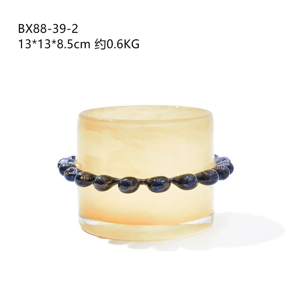 A dark blue glossy glass bead bracelet with golden flecks paired with a glass cylinder vase with black beaded rim