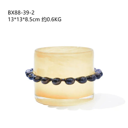 A dark blue glossy glass bead bracelet with golden flecks paired with a glass cylinder vase with black beaded rim
