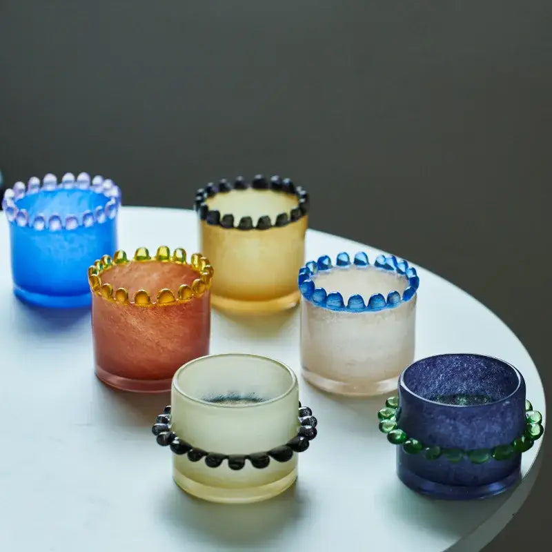 Amber glass cylinder vase with black beaded rim and colorful glass candle holders featuring blue orange yellow and purple hues