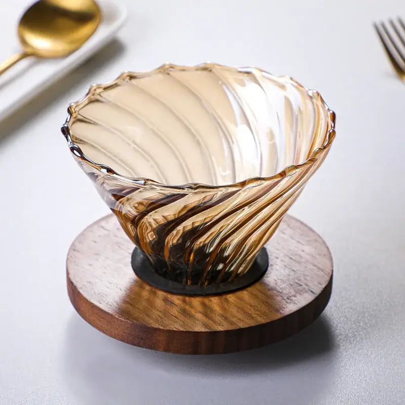 Amber glass fluted coffee filter pot with swirling ribbed design and scalloped rim on a circular wooden coaster