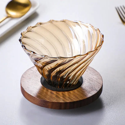 Amber glass fluted coffee filter pot with swirling ribbed design and scalloped rim on a circular wooden coaster