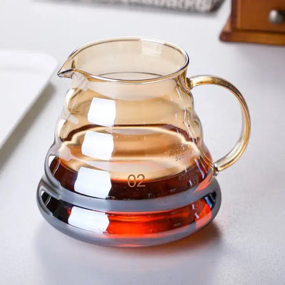 Amber glass fluted coffee filter pot with curved handle and measurement markings filled with dark liquid for pour over