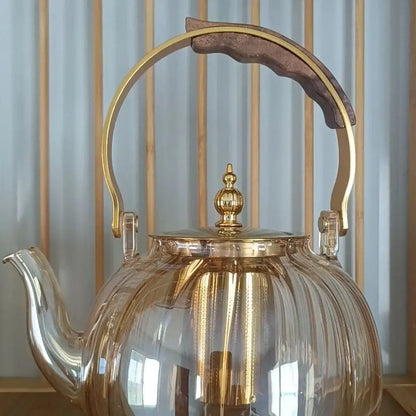 Clear glass teapot with gold-toned metal handle and lid featuring wooden grip for decorbites amber glass teapot use