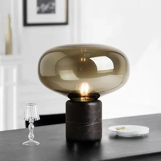 A sleek nordic table lamp with a translucent amber glass dome and a dark marble base for modern interiors