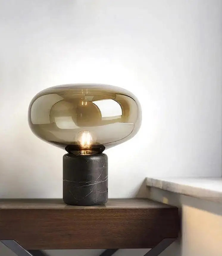 A sleek amber nordic table lamp with tinted glass shade and dark marble base for modern lighting decor