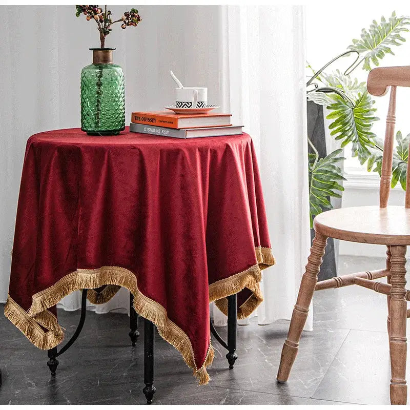 A rich burgundy table cloth with gold fringe trim made of velvet ideal for decorbites gold velvet wedding and dining room decor
