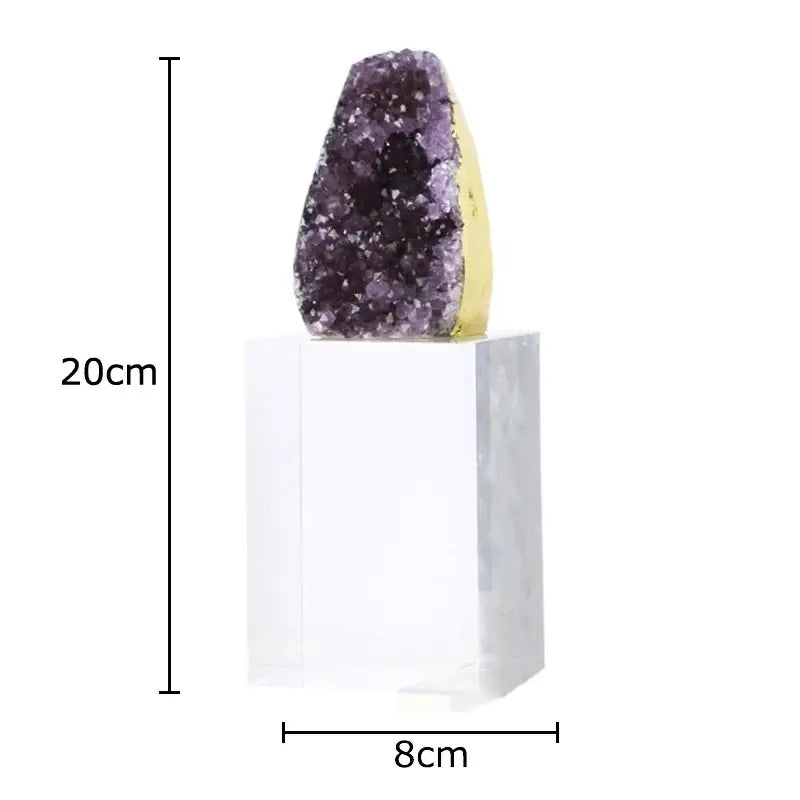 A striking purple amethyst crystal base geode with a golden base displayed as a desk ornament on a clear acrylic pedestal