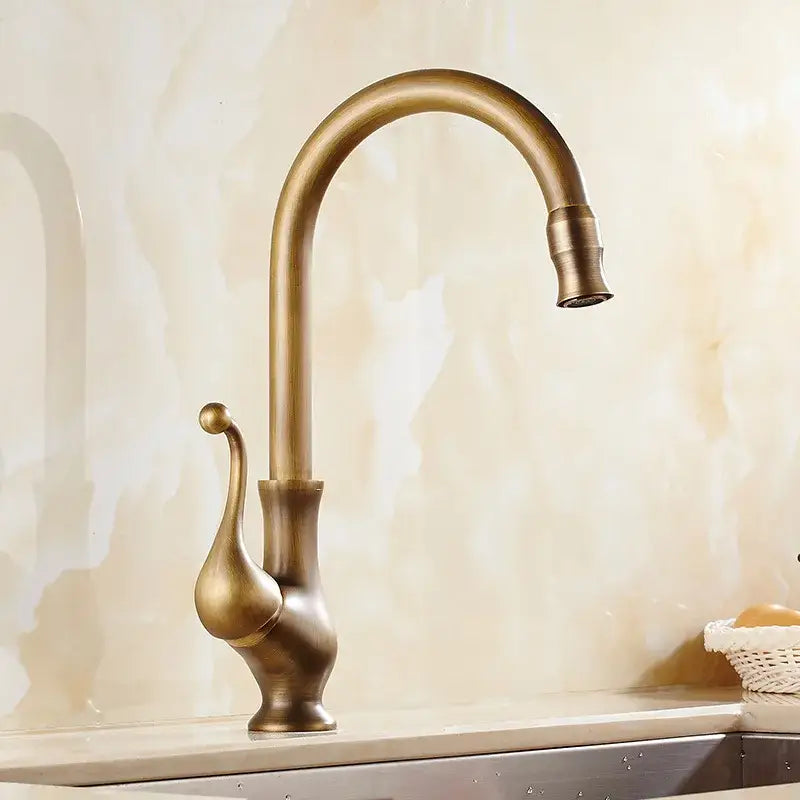 Antique brass and white ceramic kitchen faucet with curved spout and ornate teardrop-shaped handle swivel mixer
