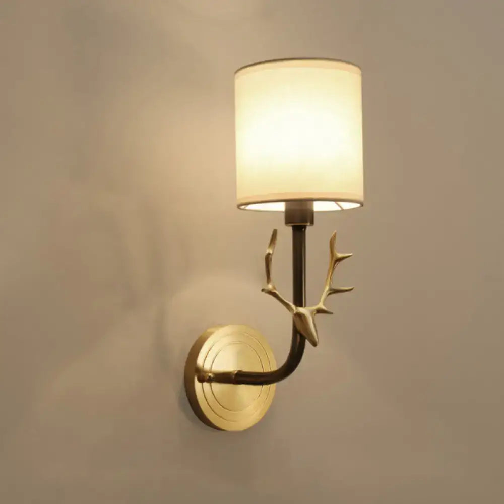 Antique brass antler wall sconce with gold-toned design and cylindrical off-white fabric shade for stylish bedroom lighting