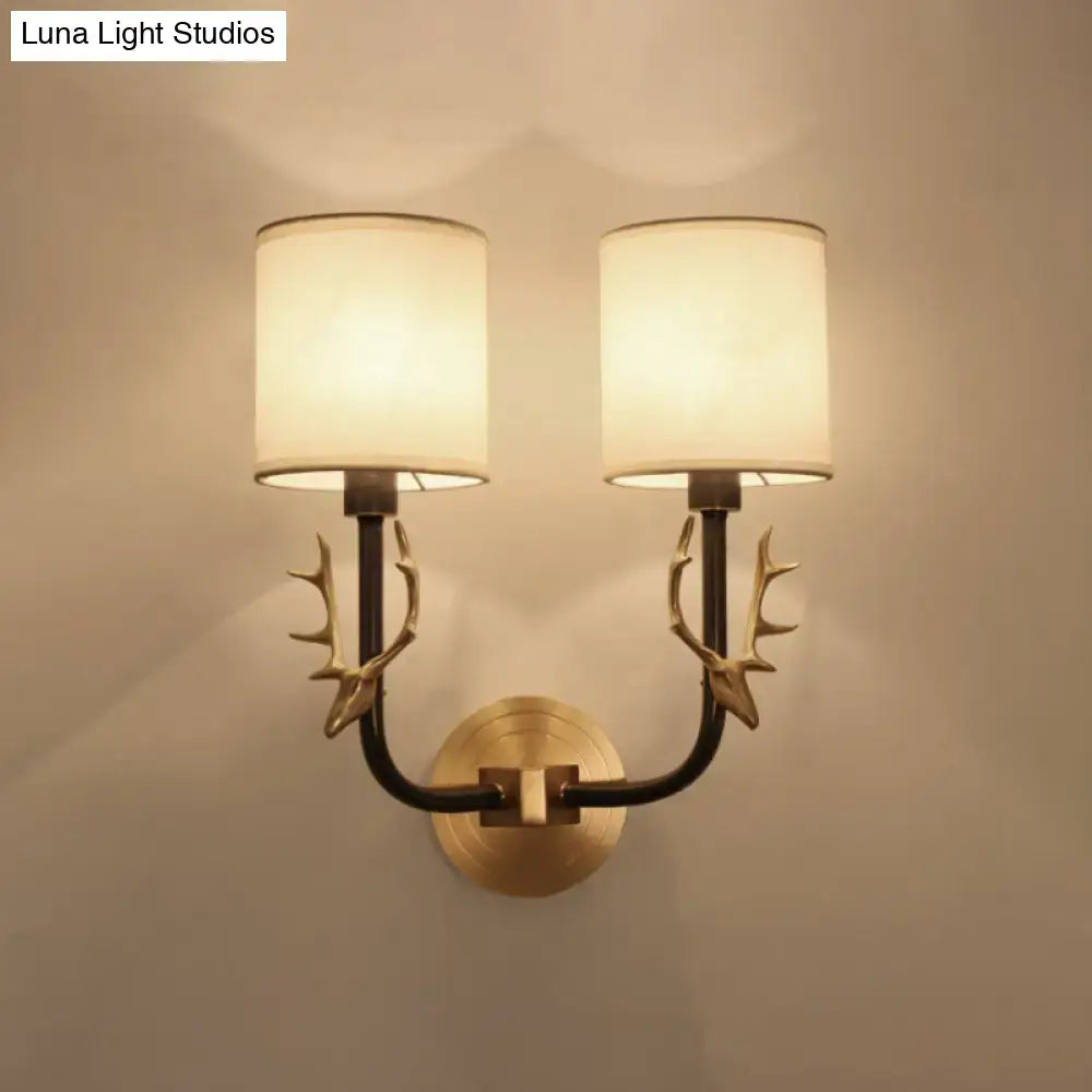 Antique brass antler wall sconce with two cream fabric shades and stylish design for bedroom lighting