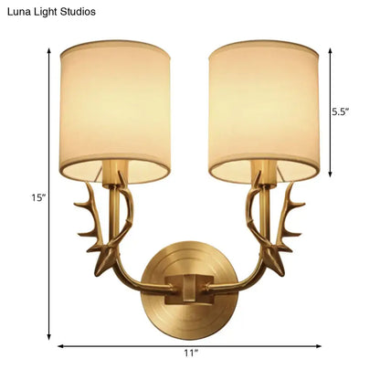Antique brass wall sconce with stylish antler-inspired arms and matching beige fabric shades for bedroom lighting