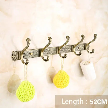 Antique brass bath hardware set featuring a wall-mounted hook rack with ornate scrollwork and five curved hooks
