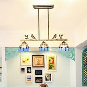 Antique brass indoor island pendant with three blue stained glass shades and decorative bird motifs