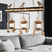 DecorBites antique brass lantern pendant with three clear glass lights, bird accent, and bulb base in rustic coastal style