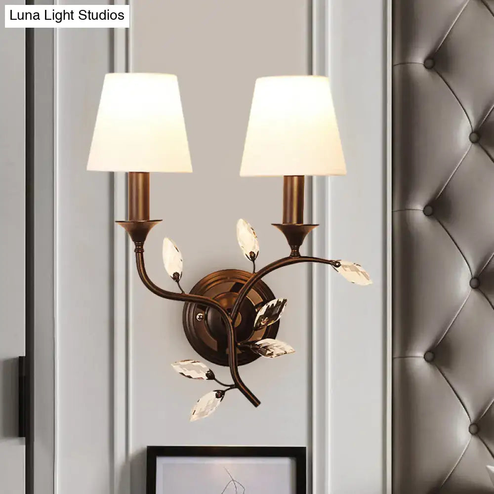 Antique brass two-light wall mount lamp with crystal leaf accents and cream fabric shades for bedroom decor