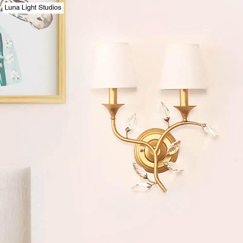 Antique brass wall mount lamp with gold-toned branch design, clear crystal leaves, and white fabric shades for bedroom use