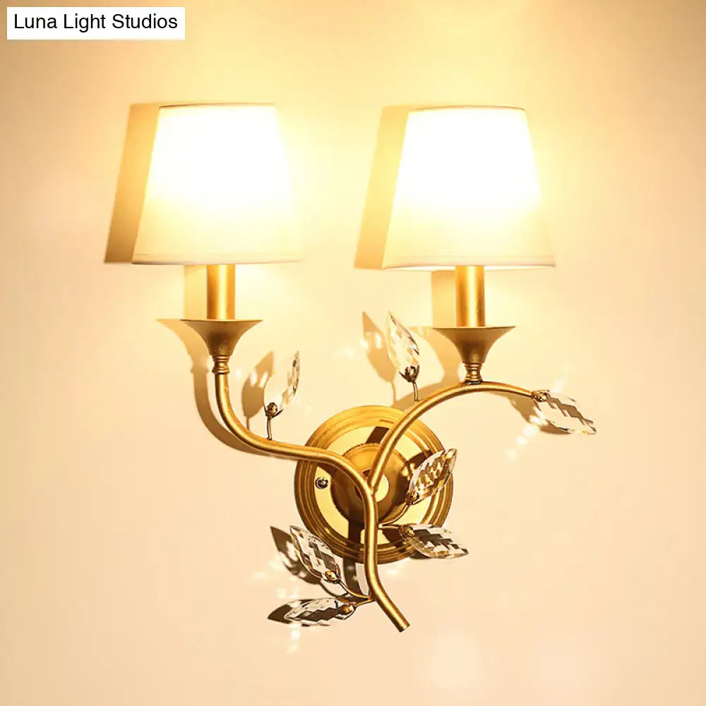 Gold-toned antique brass wall mount lamp with two lampshades and crystal leaf accents for bedroom decor
