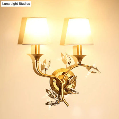 Gold-toned antique brass wall mount lamp with two lampshades and crystal leaf accents for bedroom decor