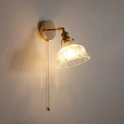 A warm-toned antique brass glass rotate copper wall sconce with ribbed translucent shade and pull-chain switch for bedroom
