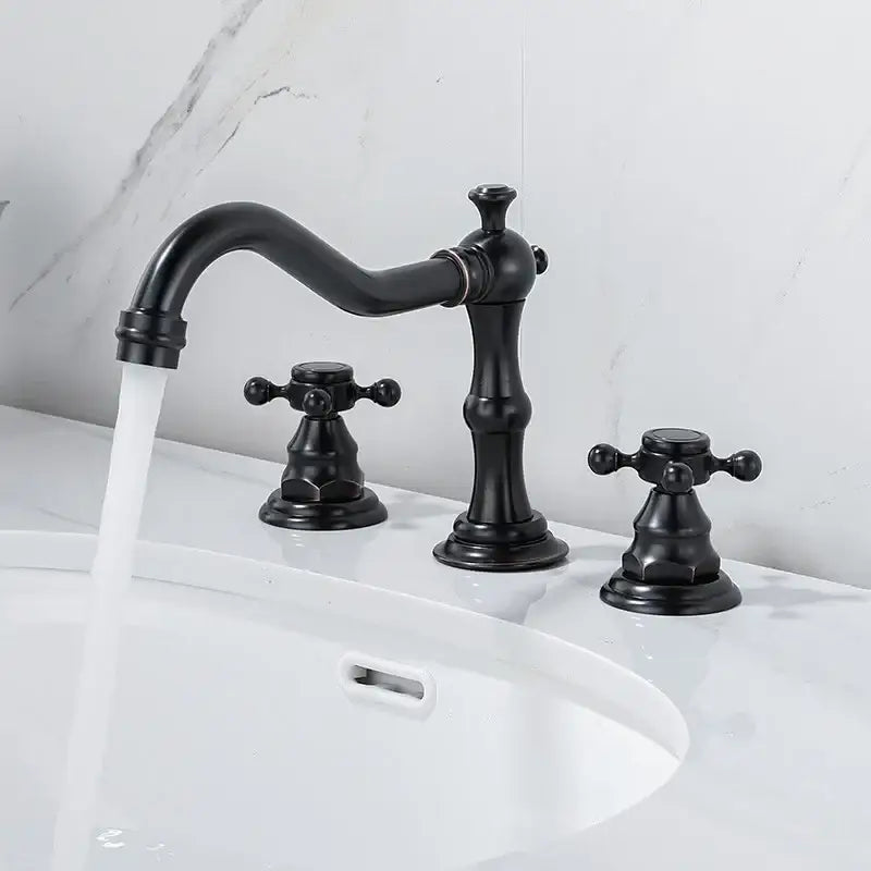 Black matte-finished brass three-handle bathroom faucet with ornate cross handles and gold finish curved spout