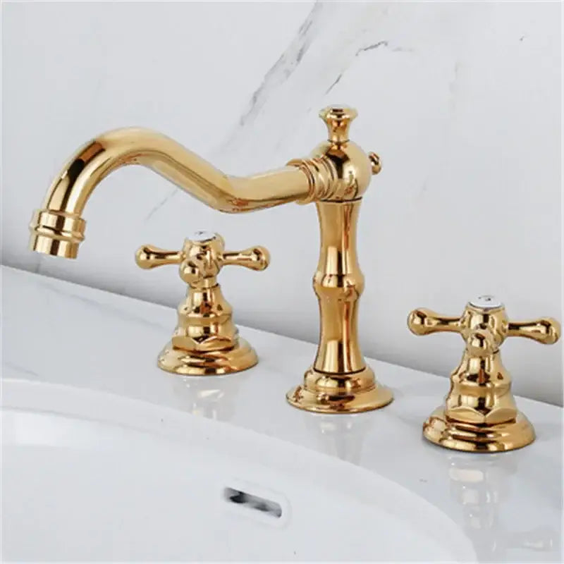 Antique brass gold finish bathroom sink faucet with ornate cross handles and a curved spout in gold finish