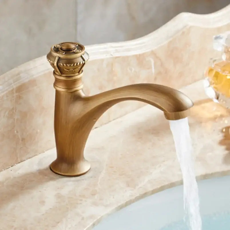 Antique brass single handle basin faucet with ornate crown-like handle and curved spout for bathroom use