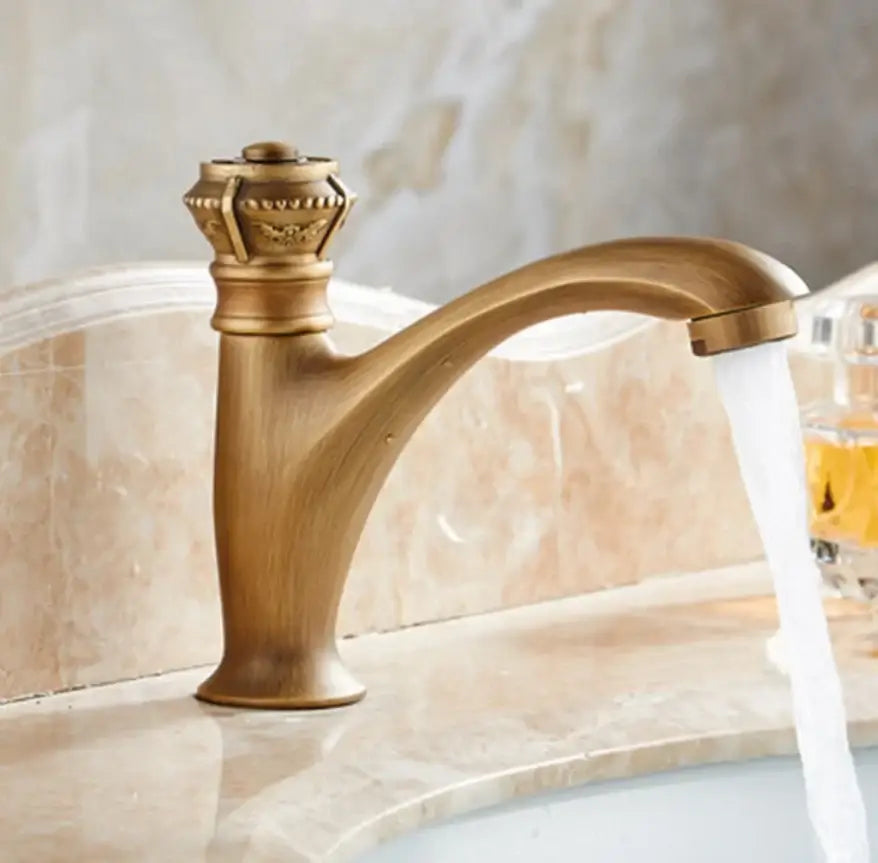 Antique brass single handle basin faucet with ornate crown-shaped handle and curved spout for bathroom use