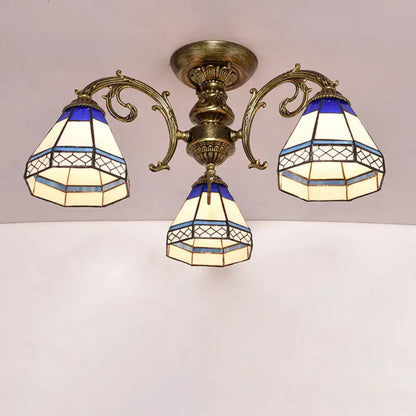 Antique brass three-arm semi flush mount ceiling fixture with blue and cream stained glass bell shades featuring geometric patterns