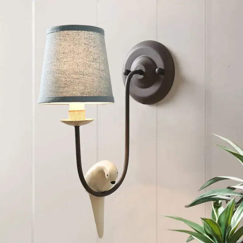 A matte black wall lamp with a gray linen shade and white ceramic bird decor by decorbites for bedroom sconce use