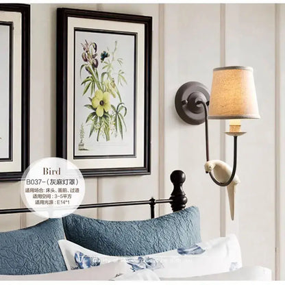 Antique bronze and cream ceramic bird wall lamp with beige fabric shade and dark metal arm for bedroom decorbites bird decor