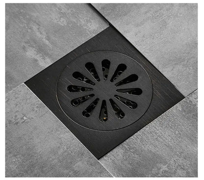 Black brass decorbites square floor drain with circular grated shower cover featuring radial slits in black brass finish