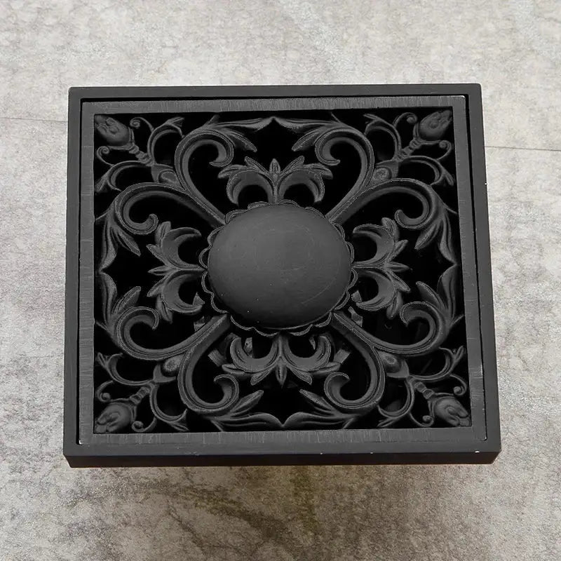 Art carved black brass shower drain cover with ornate floral and scrollwork design by DecorBites