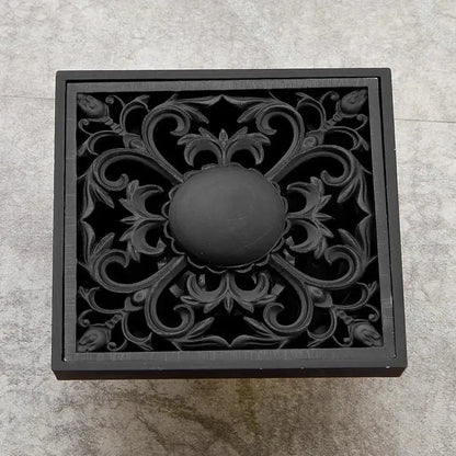 Art carved black brass shower drain cover with ornate floral and scrollwork design by DecorBites