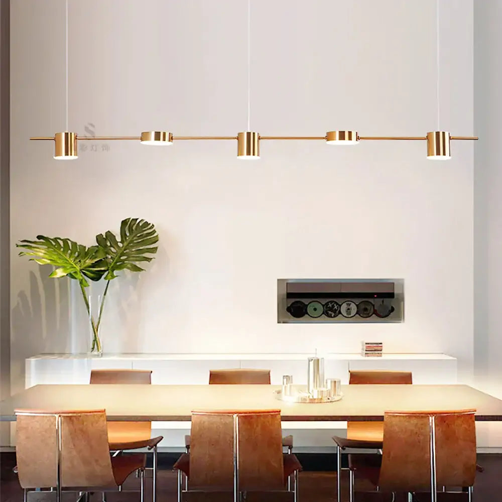 Modern gold-toned art deco pendant light with cylindrical light sources suspended above a dining table