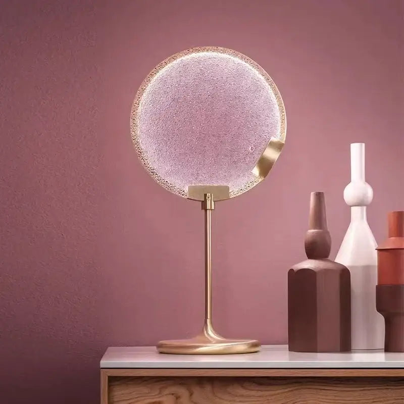 Circular vanity mirror with textured frosted glass and gold-toned frame paired with decorbites clear pink glass pendant light