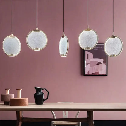 Five modern pendant lights with clear pink glass shades and gold metal frames hang against a pink wall decorbites clear pink