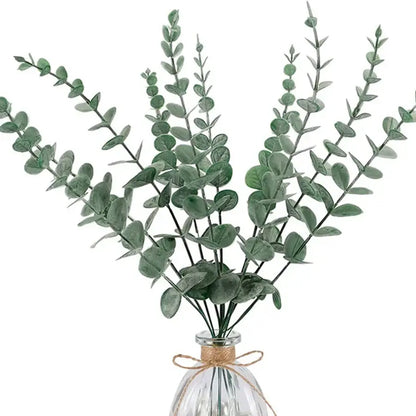 A bundle of artificial eucalyptus greenery stems with round green leaves in a clear glass vase tied with twine