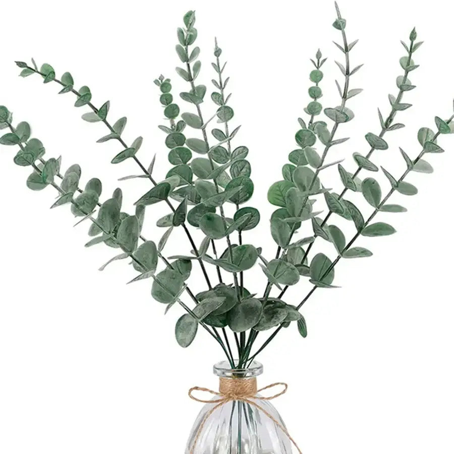 A bundle of artificial eucalyptus greenery stems with round green leaves in a clear glass vase tied with twine