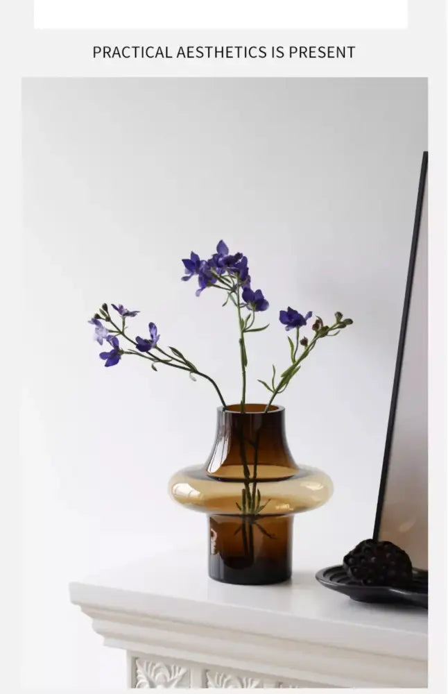 A sleek amber-tinted artisan glass vase with modern tiered design holding delicate purple flowers for elegant decor