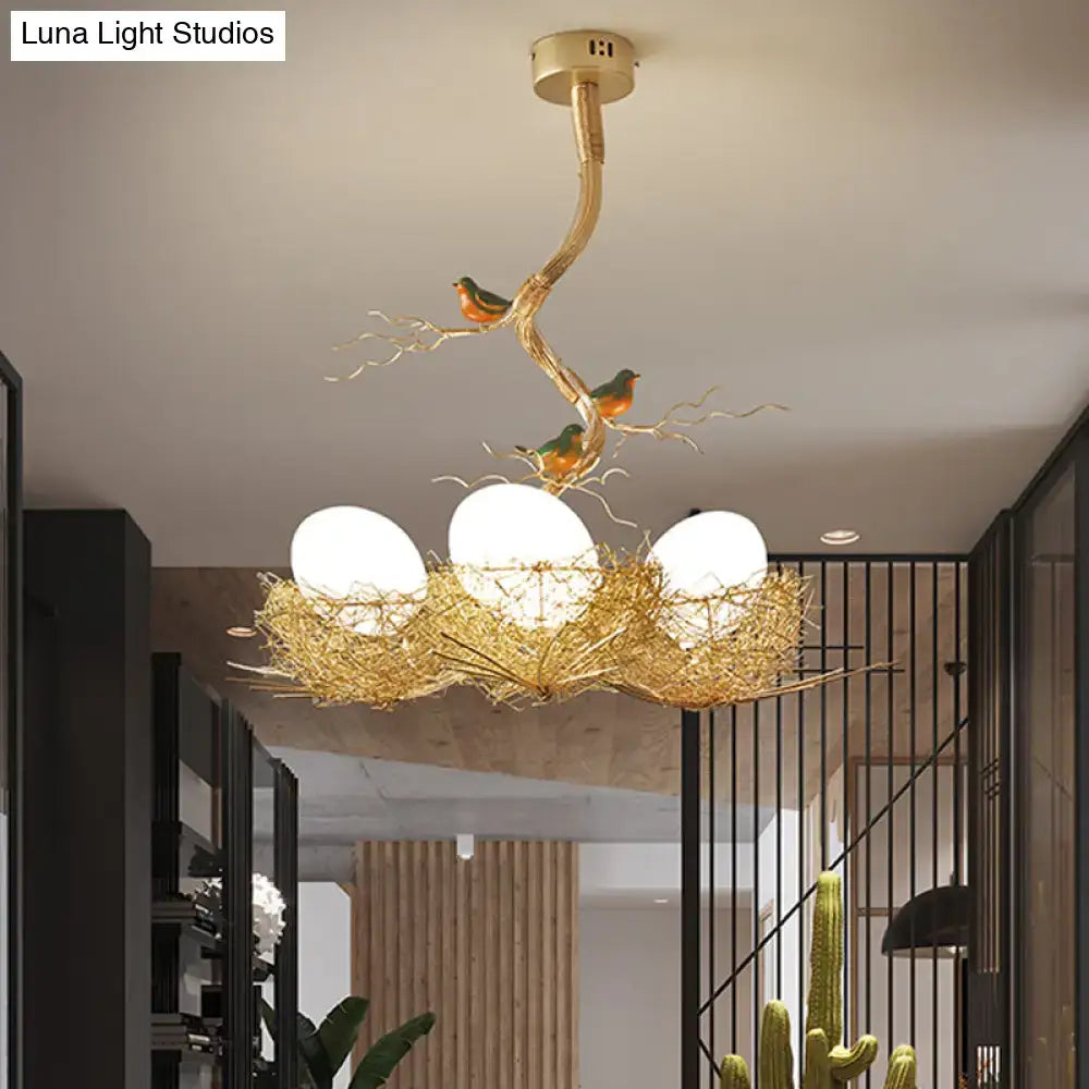 Golden bird-themed chandelier pendant with three milk white glass bulbs in a hand sewn aluminum nest design