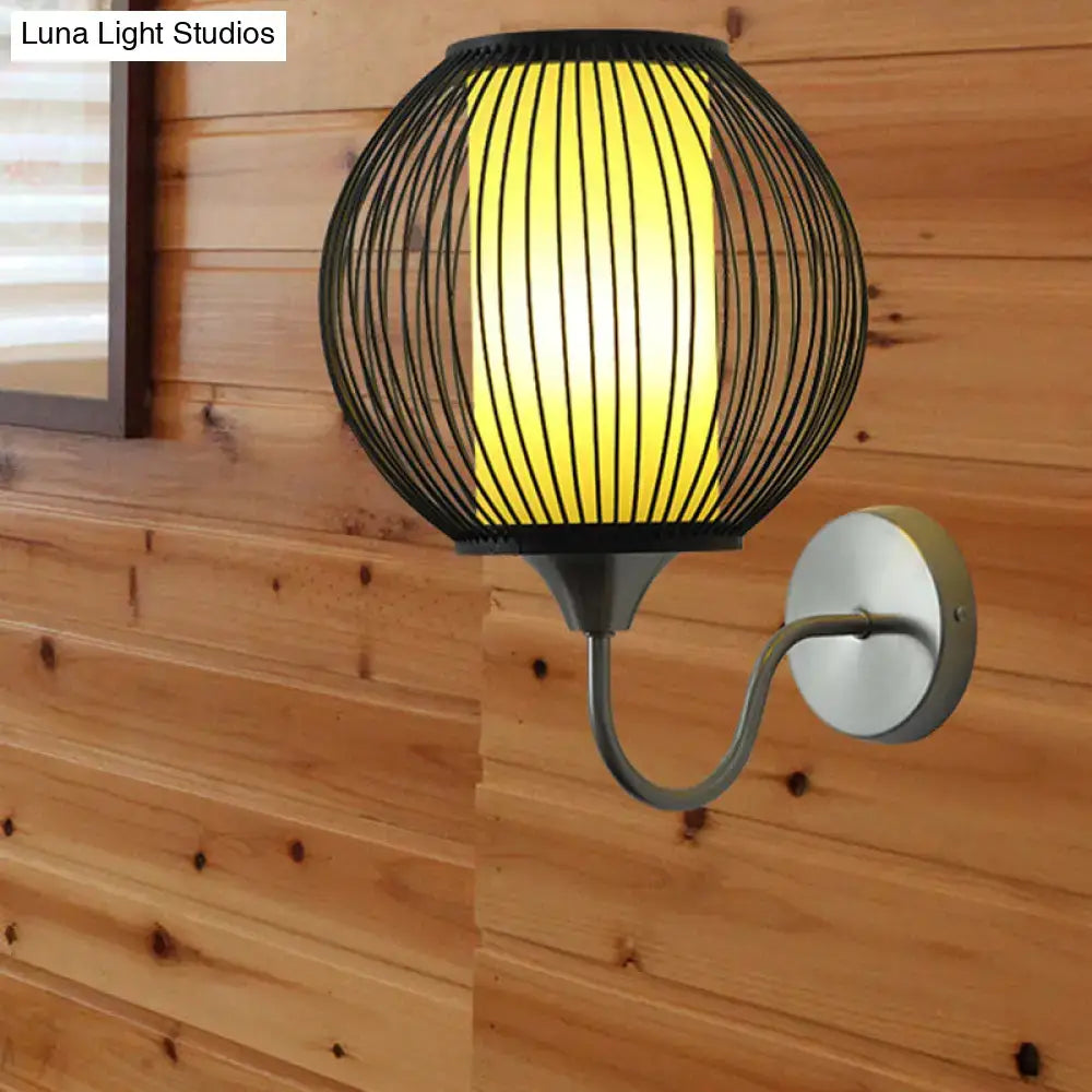 Asian style black bamboo wall lamp featuring a black wireframe spherical wall light with a warm yellow illuminated panel and gooseneck arm