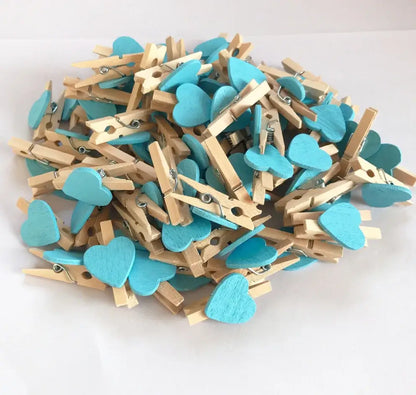 A pile of turquoise heart-shaped mini wooden clips with natural wood accents and metal springs for photo decor