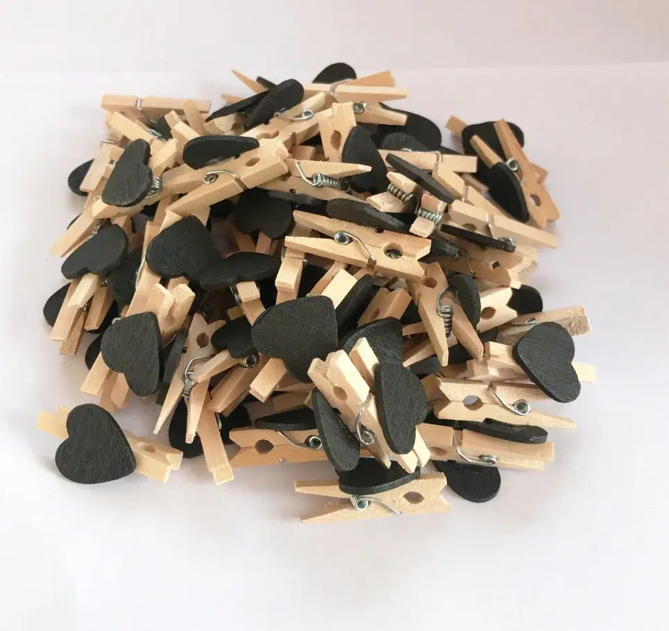 A pile of mini wooden clips shaped like hearts with black painted centers and metal springs for photo decor