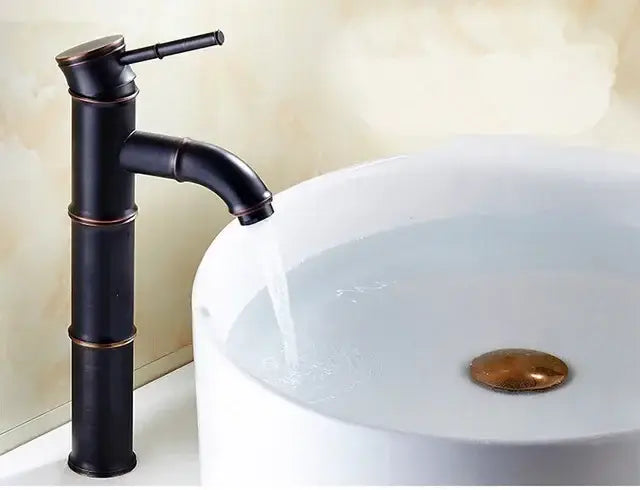 Black bamboo style high arch mixer bathroom faucet with bronze accents flowing water into white ceramic sink